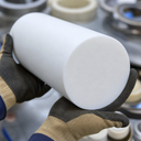 Tan and brown gloves holding a large white PTFE billet end-on, white rings behind
