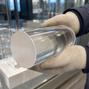 Cream-gloved hands holding a clear acrylic rod end-on in a showroom, satin cut face to the left