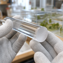 Clear transparent acrylic rod held in white knitted gloves, polished end face catching the light