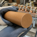 Orange-brown phenolic laminate rod cradled in navy and cream gloves, cloth weave across the sawn face