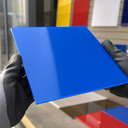 Gloved hands holding a glossy blue A4 acrylic panel with coloured sample sheets behind