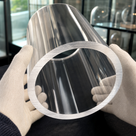 Wide clear acrylic tube held in white knitted gloves, brushed sawn ring to the front, glazed cabinets behind
