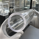 White-gloved hands holding a large clear acrylic tube with a thick sawn end, display cabinets behind.