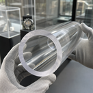 White-gloved hands holding a large clear acrylic tube with a thick sawn end, display cabinets behind.