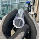 Gloved hands holding a clear acrylic tube with the bore to camera, glass tanks and pipework behind.