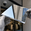 Mirror-finish acrylic sheet held outdoors, reflecting the street and shopfront