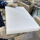 Knit-gloved hands holding a thick milky white polyethylene slab on site, concrete formwork behind