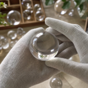 Clear acrylic sphere held between gloved fingers with more spheres behind