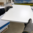 Gloved hands holding a white corrugated sheet, fluted core visible along the near edge