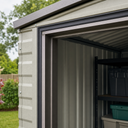 Corner of a grey metal storage building, dark seal running round the open door frame with shelving inside