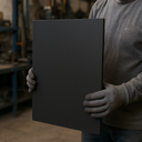 Worker in grey gloves holding a large black rubber sheet upright in a workshop, racking blurred behind