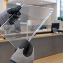 Clear acrylic screen panel held by a gloved hand in an office setting