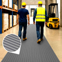Two workers walk along grey ribbed PVC matting in a warehouse aisle beside shelving and a forklift.