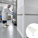 White angle trim capping a wall corner in a food plant, worker at a stainless door, inset of the profile