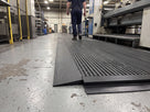 Black PVC ramp edging fitted along the exposed edge of open-rib matting in a factory walkway