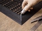 Cold weld paste being applied to a mitred corner joint in PVC ramp edging, with knife and rule alongside