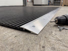 Aluminium ramp edging strip screw-fixed along the edge of an open-grid industrial mat