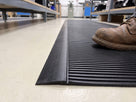 Low-profile black PVC edging ramp fitted to a 10mm ribbed anti-fatigue mat