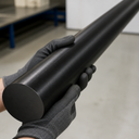 Black acetal rod cradled in grey gloved hands, matte circular end face towards the camera in a workshop