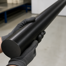 Black acetal rod cradled in grey gloved hands, matte circular end face towards the camera in a workshop
