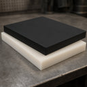 Black acetal slab stacked on a natural-white slab on a steel workshop bench, thick sawn edges