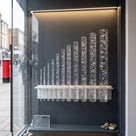 Row of clear acrylic bubble rods in graduated diameters standing in a lit shop window display, bubbles visible in each