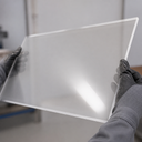 Clear acrylic sheet held by gloved hands against a plain indoor background
