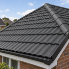 Dark slate grey painted roof tiles, close view along the hip with black fascia and gutter beneath