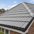 Light grey painted roof tiles on a hipped roof, ridge tiles catching the sun above a white soffit