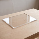 Clear acrylic panel resting on a pale birch plywood table, grain showing straight through it, bright sawn edge