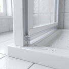 Clear tapered blade seal in a white bifold door bottom rail, meeting a white tray dotted with droplets