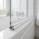 White seal with a hollow curled foot under a bath screen rail on a white bath, taps behind