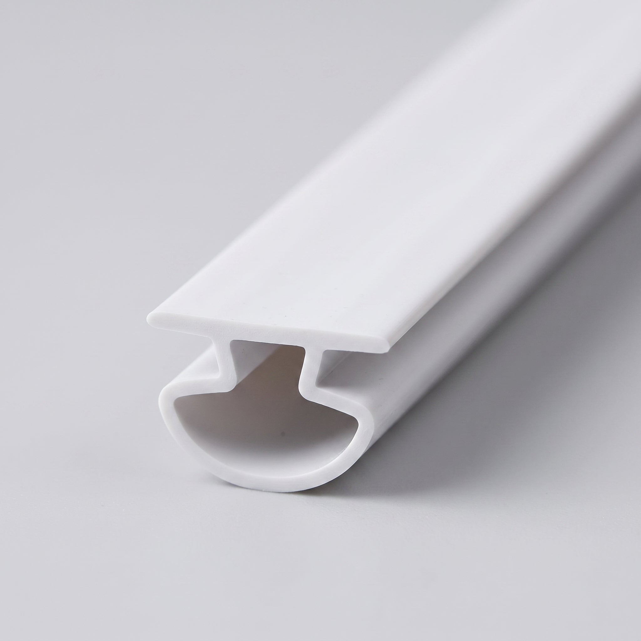Studio shot of the white bifold seal profile - thin 8mm T-cap on a hollow rounded bucket base, 6mm overall, soft white PVC