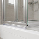 Clear seal beneath the brushed aluminium bottom rail of a folding shower door on a white tray