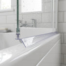 Clear seal with a down-angled blade under a white bath screen rail, sloping to the white bath below