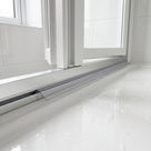 Slim clear blade seal in a narrow aluminium rail beneath a white bifold door, wet tray below