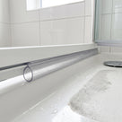 Clear oval-loop seal along a bifold door bottom rail, resting on a white shower tray beaded with water