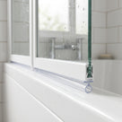 Clear seal with a small round bubble under a white bath screen rail, water beaded on the glass above