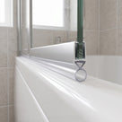 Clear ring-bubble seal under the silver rail of a bath screen, on a white bath with beige tiles behind