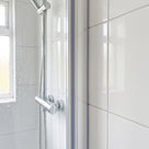 Slim clear seal down a shower screen upright against white gloss tiles, chrome bar valve and hose behind