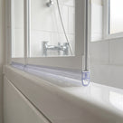 Clear tub seal along the bottom rail of a white folding bath screen, chrome bath taps behind