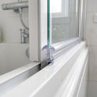 Clear tee cushion seal wedged between the glass and white frame on a bifold shower door bottom rail