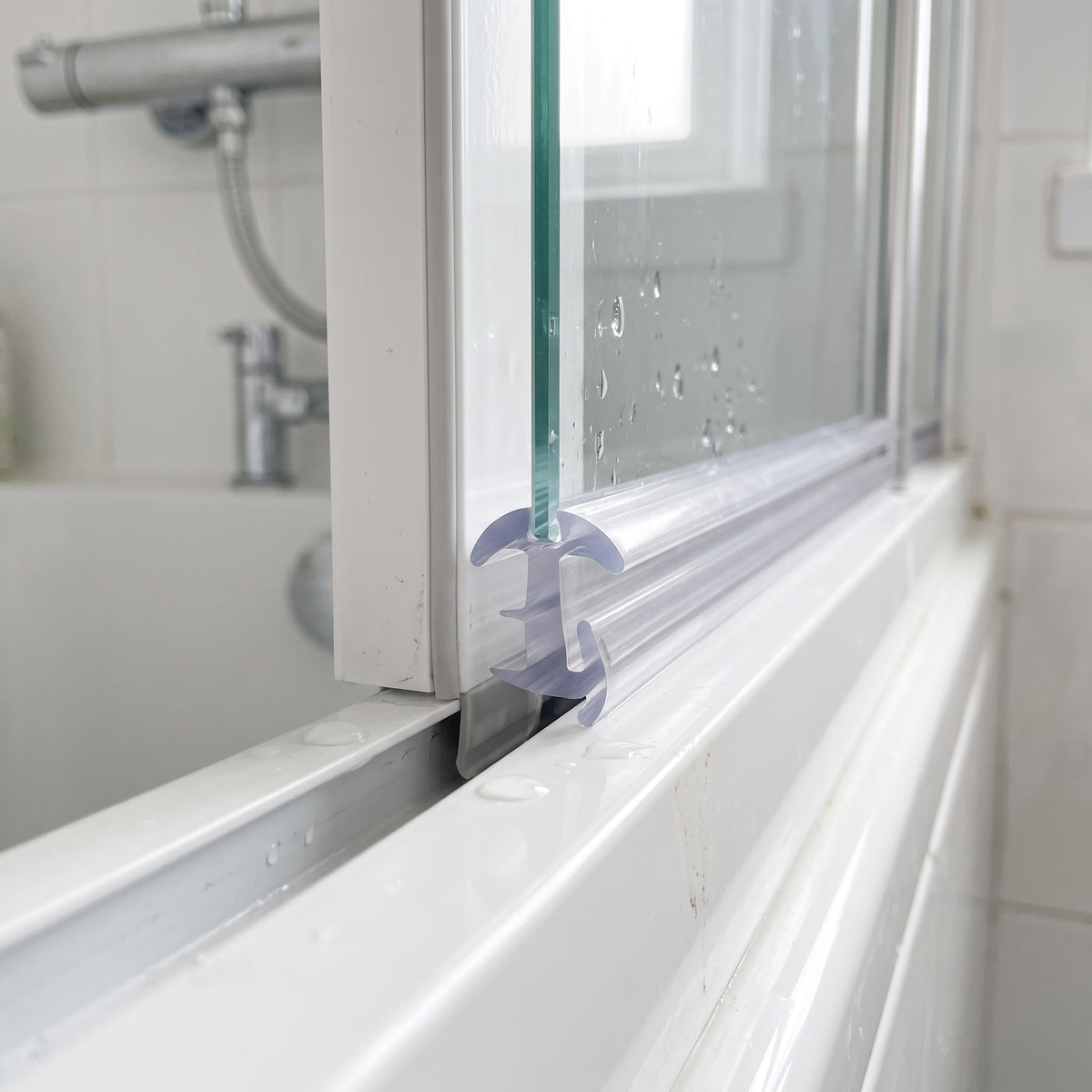 Clear tee cushion seal wedged between the glass and white frame on a bifold shower door bottom rail