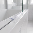 Clear low seal lying along the top face of a bath screen rail, glass above and droplets around
