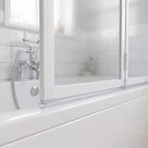 Low clear seal along the rail of a white folding bath screen, chrome bath mixer and metro tiles behind