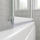 Clear seal under the bottom rail of a bath screen on a white bath, metro tiles and window behind