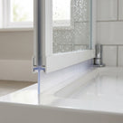 Clear straight-blade seal under the rail of a white folding bath screen, reaching down to the white bath