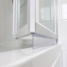 Clear blade seal under the bottom rail of a white bifold bath screen, meeting the glossy tray edge