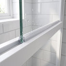 Clear frame seal along the bottom rail of a white shower screen, water droplets on the glass above