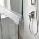 Clear ribbed frame seal on the top rail of a glass shower screen, chrome shower valve and hose behind